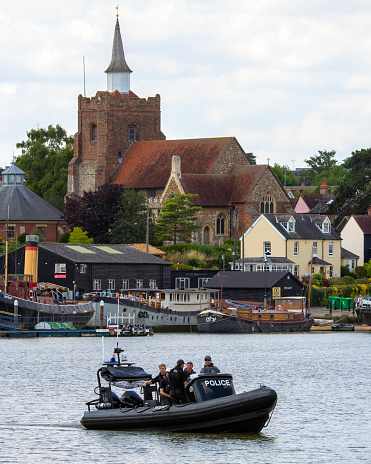Essex, UK - July 13th 2022: A Police boat on the river Chelmer with St. Marys Church in the background, in the town of Maldon in Essex, UK.