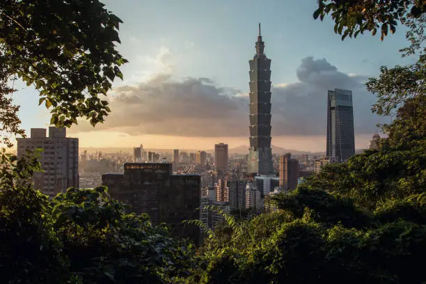 Elevated view from Xiangshan Elephant Mountain on Taipei 101 at sunset with blue sky and some clouds.
