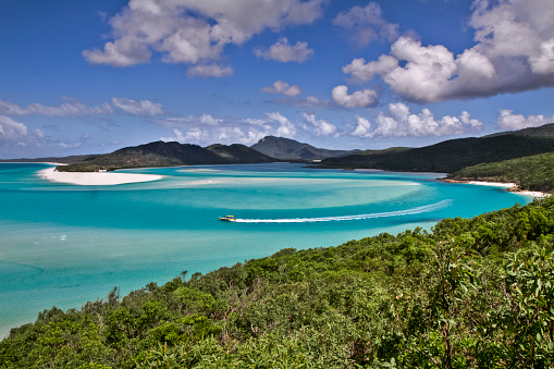 Elevated view of Whitehaven Beach at Whitsunday Islands with blue sky, some clouds and a yellow boat cruising through