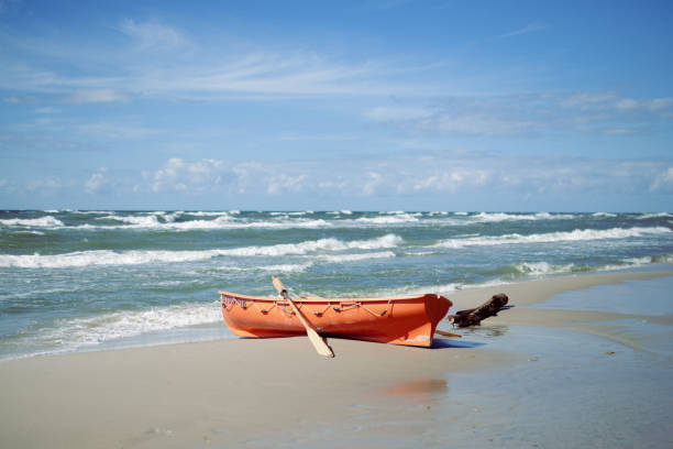 A small orange boat on a sandy beach facing a calm blue sea on a sunny summer day, symbolizing vacation, relaxation and freedom.