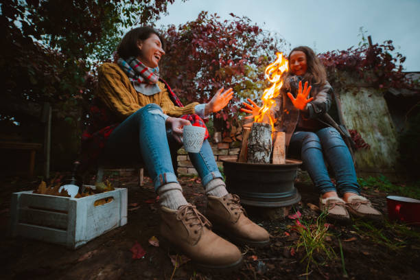 3人の友人が快適にリラックスし、裏庭の暖炉のそばの野外で秋の夜にワインを飲みます。 - comfortably ストックフォトと画像
