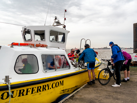 Cyclists and ferry boat staff loading cycles onto the Harwich Harbour Foot Ferry at Shotley Gate in Suffolk, Eastern England, in preparation for the journey to Harwich in Essex, which is on the horizon. The ferry also serves Landguard Point in Felixstowe.
