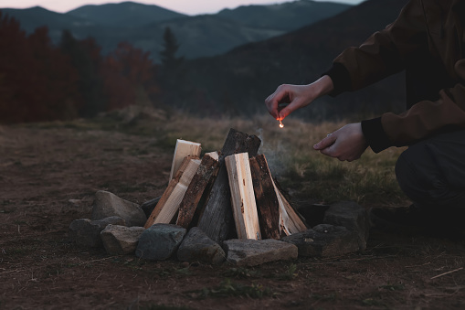 Traveler lighting up bonfire with matches outdoors in evening, closeup