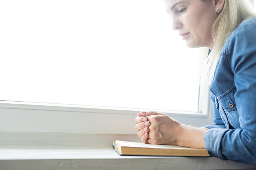 Hands of woman with Bible praying.