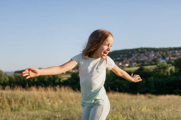 Happy girl having fun running and spinning at the meadow with her arms outstretched