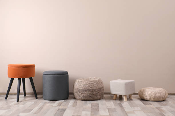istock Different stylish poufs and ottomans near beige wall, space for text 1408628595
