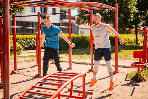 Two handsome young men training outdoors in a park. Doing jumping squats.