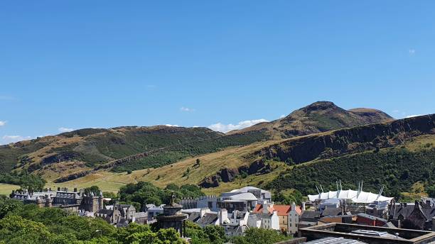 Edinburgh, Scotland, UK - August 3, 2024: Edinburgh during the Edinburgh Fringe Festival. There are people walking or relaxing near the Scottish Parliament Building. At the background Arthur's Seat