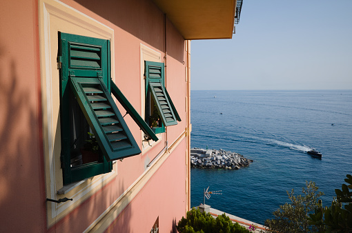 Pink building facade with green shutters on windows in typical Italian style. Traditional italian house on Mediterranean shore, Camogli, Liguria, Italy. Windows of house overlooking Ligurian Sea