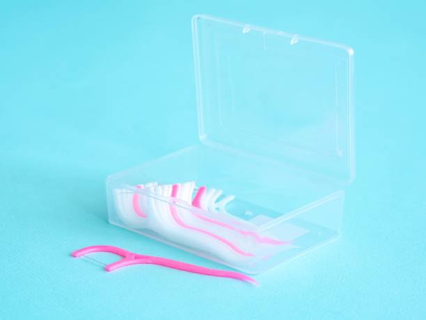 istock Dental floss with a plastic toothpick in white and pink in a plastic transparent container on blue. Dental concept 1408635272