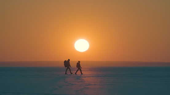 The romantic couple walking through the snow field on sunset background
