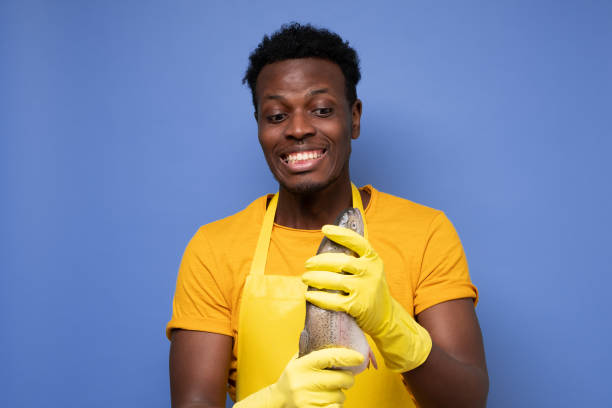 istock African young cook holding a fresh fish on a purple background 1408643429