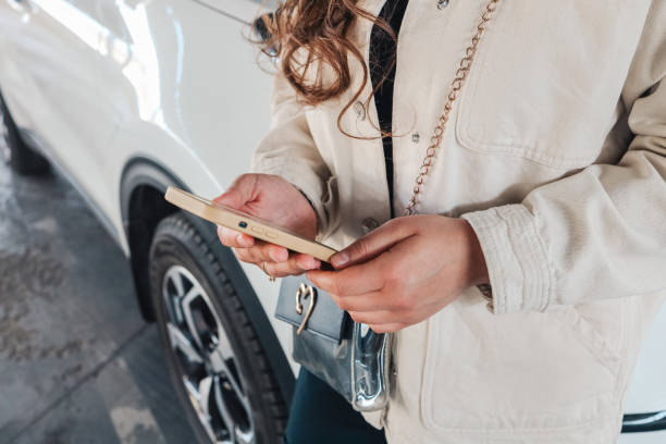 женщина, использующая телефон перед автомобилем - car insurance фотографии стоковые фото и изображения