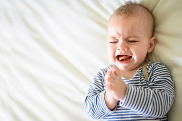 Adorable baby boy crying in white sunny bedroom in the morning at home An Adorable baby boy crying in white sunny bedroom in the morning at home bear stomach stock pictures, royalty-free photos & images