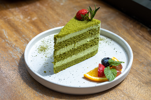 Green cake on a white plate decorated with fruit with wooden background