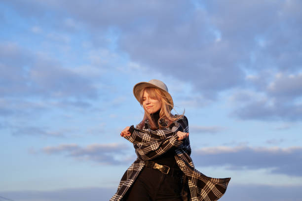 Young girl in hat, black jeans and shirt dancing feeling joyful or carefree emotion in front of blue cloudy sky. Winning, expressive or positive concept. High quality image
