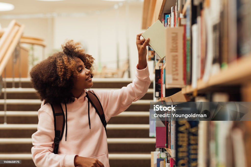 Girl taking a book from bookshelf in library Library Stock Photo