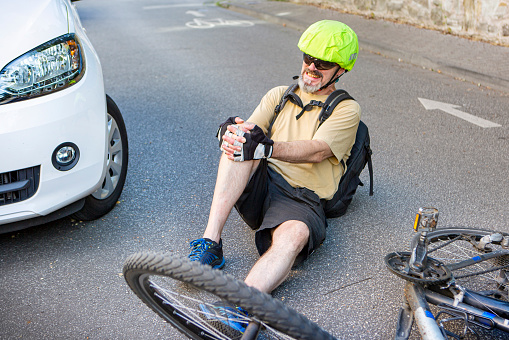 Male cyclist sitting on the road with pain in his knee, after he fell of his bicycle. Bicycle accident, injured knee.