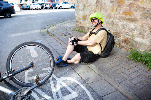 Male cyclist sitting on the road with pain in his knee, after he fell of his bicycle. Bicycle accident, injured knee.