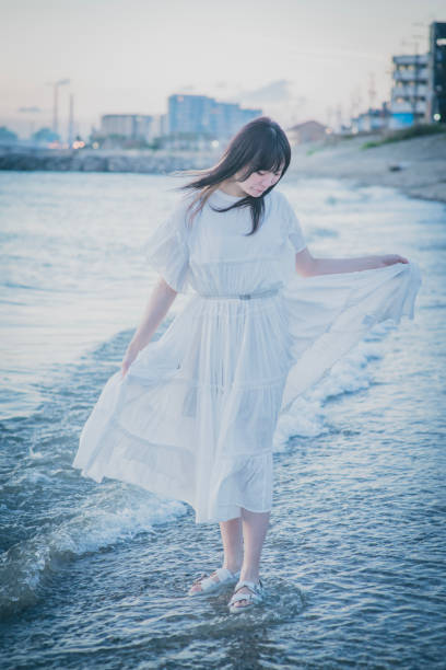 Woman with Arms Outstretched Standing Confidently in White Top with Majestic Wind Turbine Towering in the Distance.