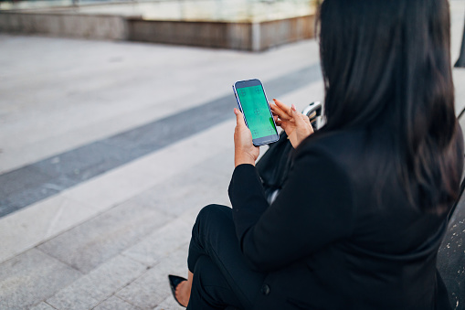 Back view of unrecognizable woman using smart phone with green screen