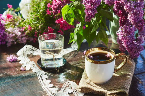 terrasse d’été avec tasse de café, verre d’eau, fleurs lumineuses d’été. brunch cottage core avec des couleurs estivales colorées du jardin par une journée ensoleillée. ombres dures - snack coffee instant coffee cappuccino photos et images de collection