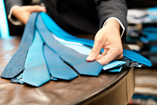 Man showing blue neckties at menswear boutique, close up of hands, unrecognizable person.