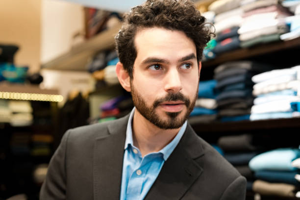 Portrait of confident young man wearing suit standing in menswear showroom and looking away.