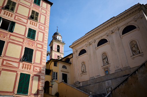 View of bell tower of church called Basilica di Santa Maria Assunta and side wall of temple with statues, Camogli, Liguria, Italy. Typical Italian buildings in small town on Mediterranean coast