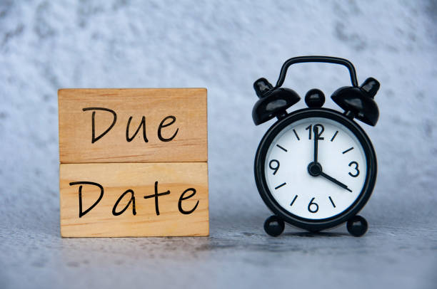 Alarm clock pointing at 4 o'clock with text on wooden block - Due Date. Time concept