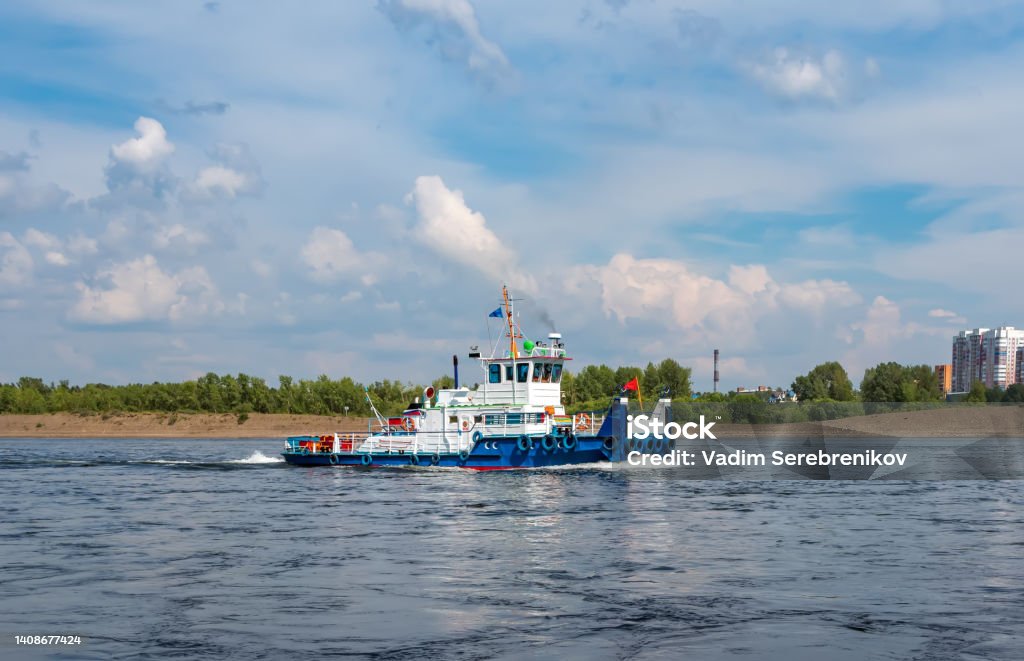 River tug boat is moving along the water against cityscape. Barge Stock Photo