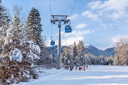 Bansko, Bulgaria - February 3, 2022: Bulgarian winter ski resort panorama with gondola lift cabins, Pirin mountain peaks view, slope and skiers