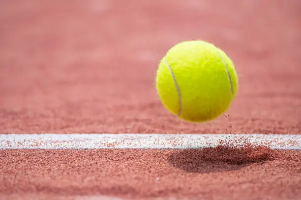 A close-up of a tennis ball in mid-air after hitting just pass the baseline on a clay court.