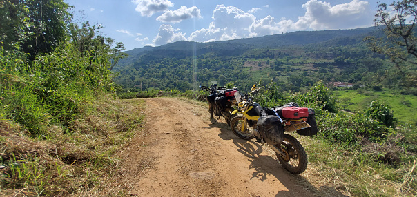 Two motorcycles on a dirt road on a sunny day with mountains around