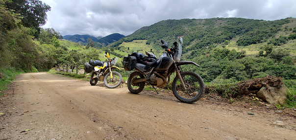 Two motorcycles on a dirt road in the middle of a mountainous landscape on a sunny day