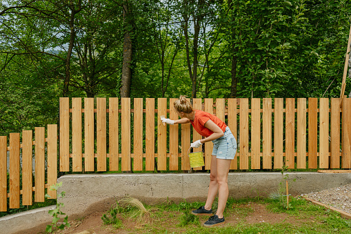 Photo of a young woman painting a picket fence