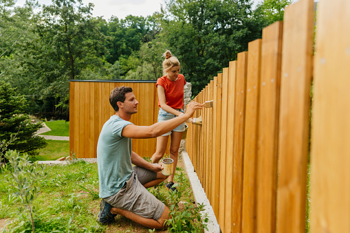 Photo of a young couple painting a picket fence