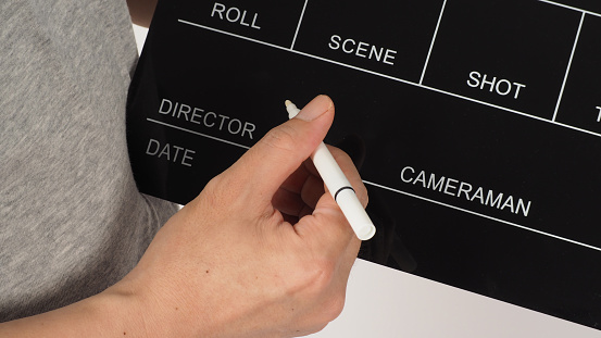 The hand is holding a black clapper board and marker Pen on white background.