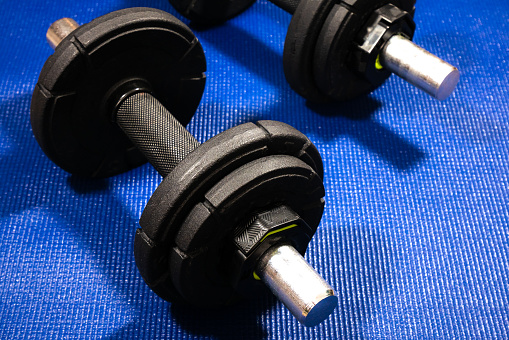 Heavy black dumbbells lying on the sports mat in the gym. Fitness sport motivation. Happy healthy lifestyle living. Exercises with bars weights. Home sport training.