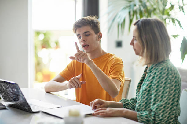 Deaf teenage boy signing while e-learning from home Waist-up view of high school student’s online education with parent assistance. Part of lifestyle series depicting deaf family and friends. sign language stock pictures, royalty-free photos & images