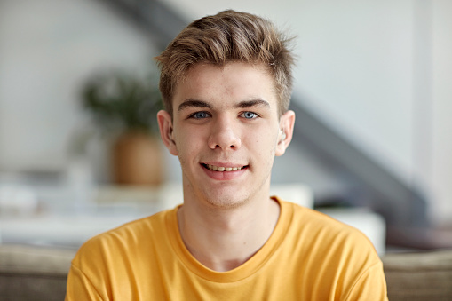 Head and shoulders view of boy with short blond hair wearing yellow t-shirt and smiling at camera. Part of lifestyle series depicting deaf family and friends.