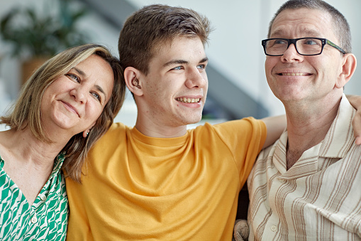 Close view of boy with arms around his mother and father, everyone smiling and looking away. Part of lifestyle series depicting deaf family and friends.