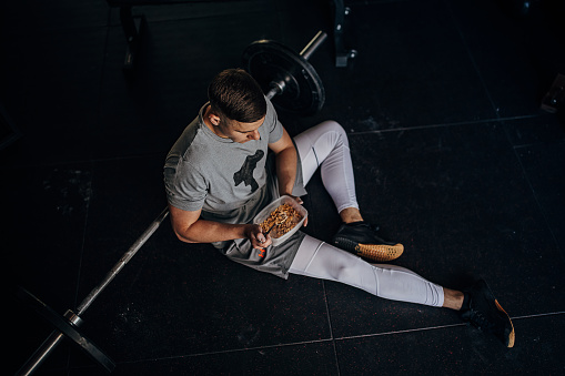 One man, fit young man on lunch break sitting on the floor in gym alone.