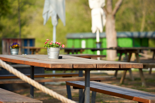 Beer garden with flowers decoration on table. Seating in the sun with plant in tin bucket.