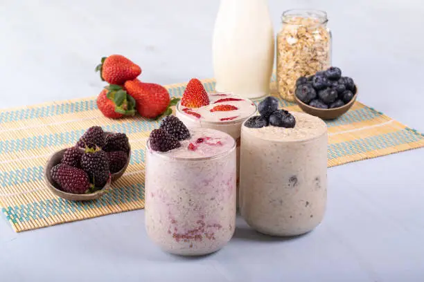 Overnight oats with fruits of blackberry, strawberries, and blueberries, accompanied by their own fruits, and milk and oats in the back.