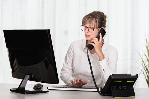 Front view of a businesswoman with eyeglass using computer and talking on the phone