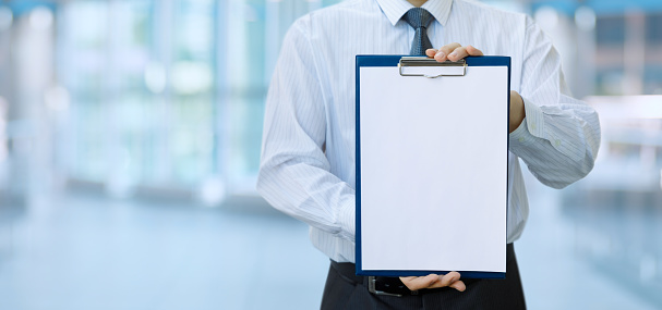 A businessman shows a blank sheet to fill out tasks on a blurred background.