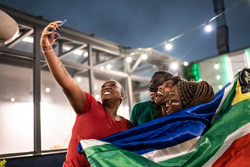 Sport fan friends taking a selfie using mobile phone in a bar