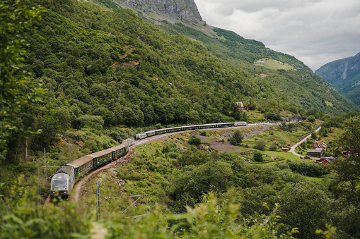 Passenger train of the Flåm Railway Line passes along a mountainside with a glacial river in the valley below. The line runs between Myrdal and Flåm in Aurland.