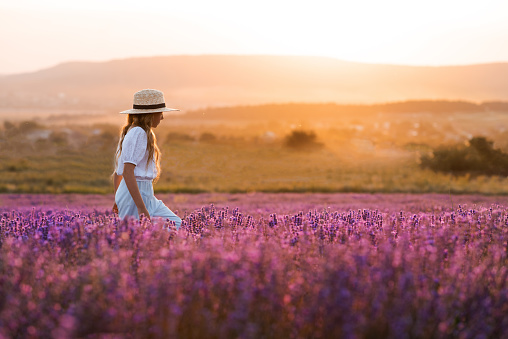 Stylish teenage girl 8-9 year old walking in blooming lavender flower field over nature sunny background outdoor. Springtime.